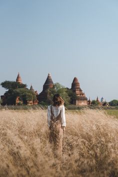 a woman walking through tall grass in front of temples