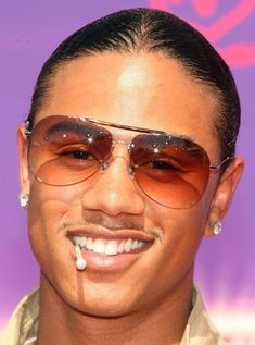 a man with sunglasses and piercings on his head smiles at the camera in front of a purple background