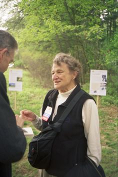 two people standing next to each other in front of trees and signs with information on them