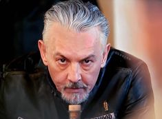 an older man with grey hair wearing a black leather jacket and looking at the camera