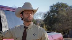 a man in a cowboy hat standing next to a red truck wearing a tan shirt and tie