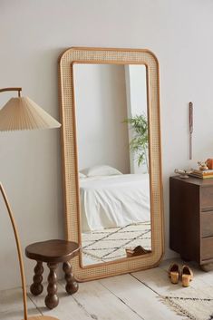 a mirror sitting on top of a wooden floor next to a lamp and dresser in a bedroom