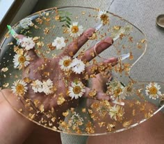 a person holding a glass plate with flowers on it and gold flakes all over them