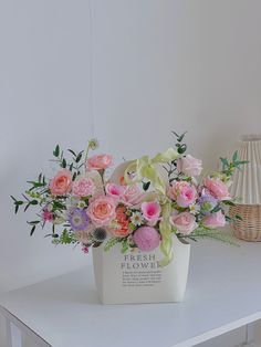 a white flower box with pink and purple flowers in it sitting on a table next to a lamp