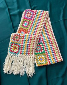 two colorful crocheted scarfs laying on top of a green cloth covered bed