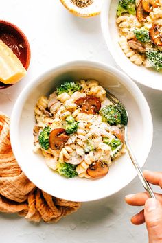 two bowls filled with pasta, broccoli and mushrooms next to some crackers