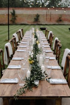 a long wooden table with candles and greenery on it is set for an outdoor dinner