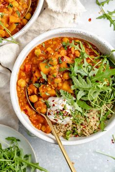 two bowls filled with vegetables and rice on top of a white tablecloth next to silver spoons