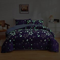 a bed covered in purple and green comforter with stars and moon designs on it