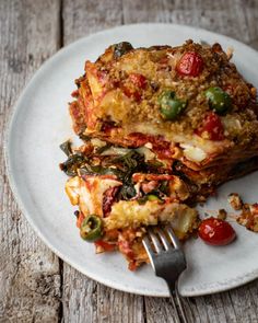 a white plate topped with lasagna covered in sauce and toppings next to a fork