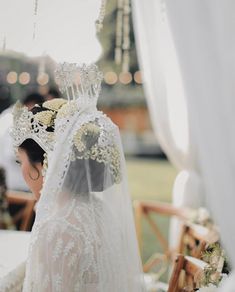 a woman in a wedding dress and veil sitting at a table with flowers on it