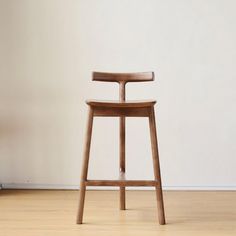 a wooden stool sitting on top of a hard wood floor next to a white wall