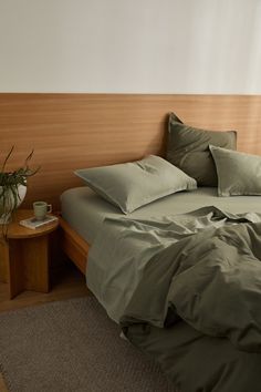 a bed with green sheets and pillows in a room next to a small side table