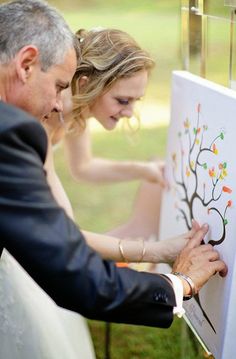 a bride and groom are drawing on a canvas together at their wedding ceremony in the park