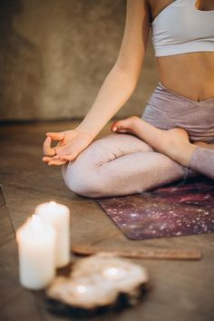 a woman sitting on the floor with her legs crossed in yoga position next to a lit candle