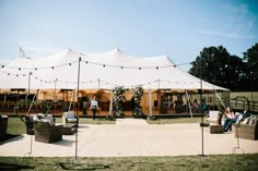 a large white tent set up with couches and chairs under string lights on the grass