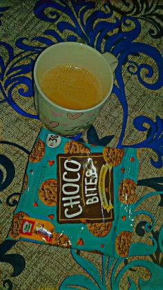 a cup of coffee sitting on top of a blue and brown mat next to a bag of cookies