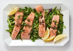 salmon and asparagus on a white plate with lemon wedges for garnish