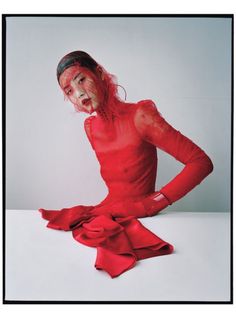 a woman in red is sitting on the floor with her hands on her hips and looking at the camera