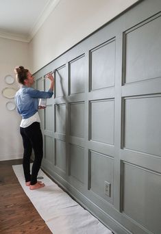 a woman is painting the side of a gray garage door with white paint on it