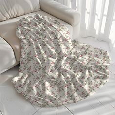 a white couch sitting next to a window covered in a blanket with pink flowers on it