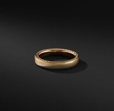 a gold wedding ring on a black surface with no one in the photo looking at it