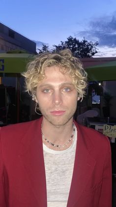 a man with blonde hair wearing a red jacket and white t - shirt is looking at the camera