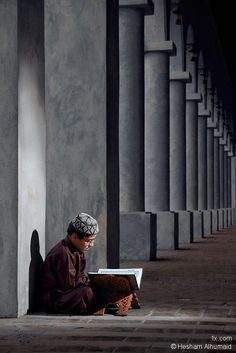 a man sitting on the ground reading a book in front of some tall pillars and columns