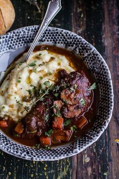 a bowl filled with meat and mashed potatoes on top of a table next to bread