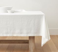 a white table cloth on top of a wooden bench in front of a bowl and cup