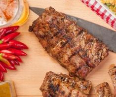 the steak is being cut into pieces on the cutting board next to some vegetables and sauces