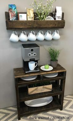 a coffee machine and some cups on a table with a potted plant next to it