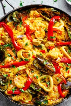 a skillet filled with seafood and rice, garnished with red bell peppers