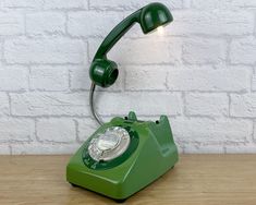 an old green telephone sitting on top of a wooden table next to a white brick wall