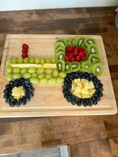 a wooden tray topped with grapes, kiwis and strawberries on top of a table