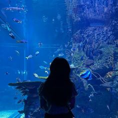 a woman standing in front of an aquarium looking at fish