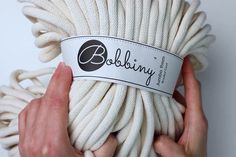 two hands holding a white ball of yarn with the label bobbiny on it