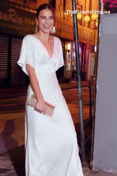 a woman in a white dress standing next to a street sign and holding a purse