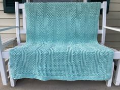 a white rocking chair with a blue knitted blanket on it's seat outside