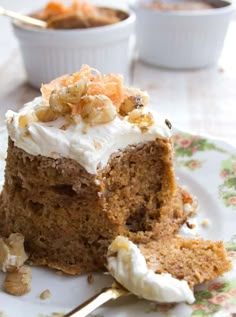 a piece of carrot cake with white frosting and walnuts on a floral plate