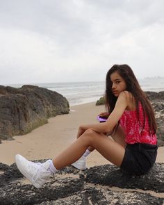 a young woman sitting on top of a rock next to the ocean holding a cell phone