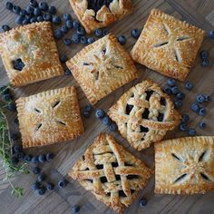 blueberry pies are arranged on a wooden table with fresh blueberries scattered around them