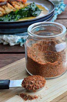 a jar filled with spices sitting on top of a wooden table next to a spoon