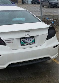 the rear end of a white car parked in a parking lot next to a chain link fence