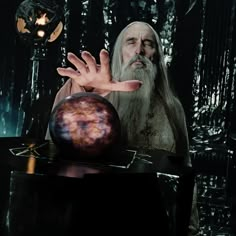 an old man with long white hair holding out his hand next to a crystal ball