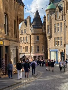 many people are walking down the street in front of some old buildings with towers on them