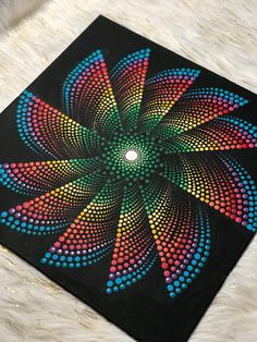 a colorful painting on a black surface that looks like an abstract flower with multicolored dots