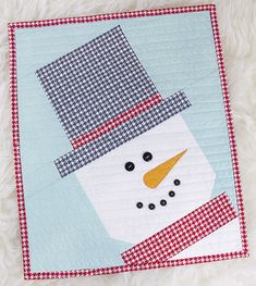 a quilted snowman on a blue and white background with red checkered border