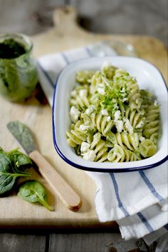 a white bowl filled with pasta and spinach on top of a wooden cutting board