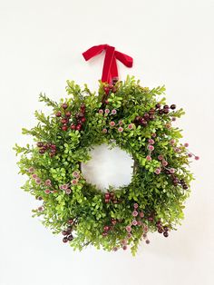 a green wreath with red ribbon hanging on the wall next to a white wall behind it